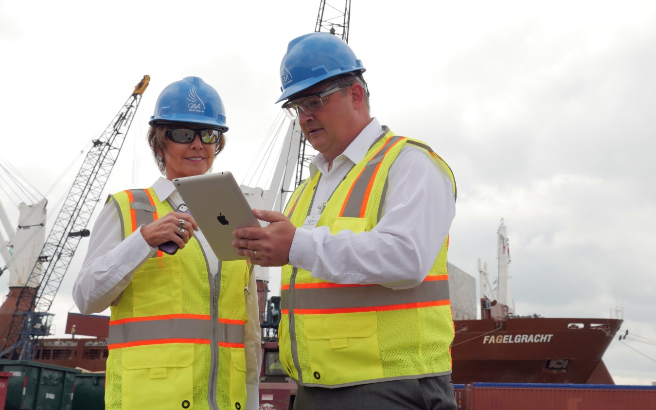 Two GAVA representatives in safety vests and hard hats reviewing shipment details at a port